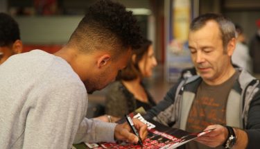 Leon Guwara unterschreibt ein Mannschaftsposter bei der Autogrammstunde für Fans mit Handicap